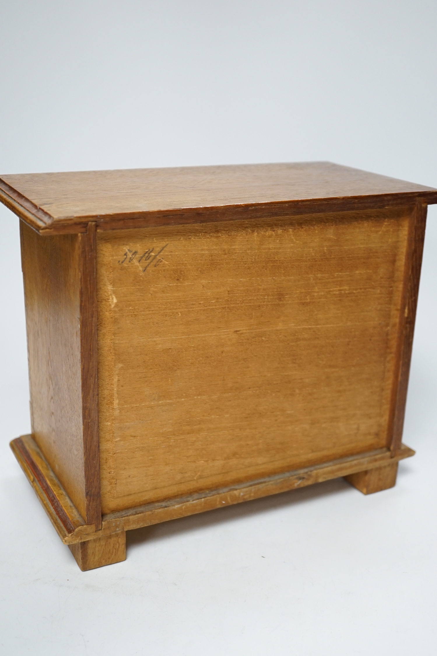 A miniature oak chest of drawers and contents (miniature bisque headed dolls and linen) height 22cm